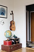Globe on top of stacked antique suitcases below guitar mounted on wall