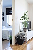 Schwarze Henkeltasche mit Tagesdecken neben Grünpflanze im Wohnzimmer und Blick ins Schlafzimmer