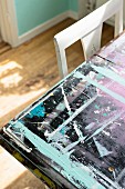 Various layers and splotches of paint on table top next to backrest of white chair