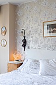 Vintage-style double bed with carved headboard below antique sconce lamp on floral wallpaper