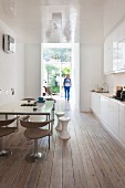 Woman walking into kitchen with high-gloss surfaces, retro chairs and wooden floor