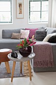 Vase of flowers on three-legged table in front of sofa with many scatter cushions