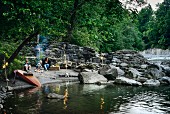 Stimmungsvolles Picknick an Flussufer mit Familie; Lagerfeuer und Windlichter auf Baumäste gehängt