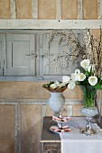 Vase of white tulips and biscuits on cake stand on console table against rustic wall