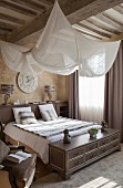 Elegantes Schlafzimmer mit aufgehängtem weißem Stoffsegel über Doppelbett an Holzbalkendecke