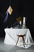 Geschirrstapel, Gläser und brennende Kerzen auf Tisch mit weisser Tischdecke