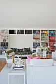 White sofa, armchairs, table and large bookcase with bench integrated into niche in background