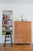 Tall chest of drawers made of pale wood next to bookshelves in niche