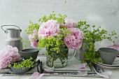 Peonies and lady's mantle in glass jug and tin utensils