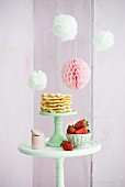 Pompoms and honeycomb ball above waffles and strawberries on table