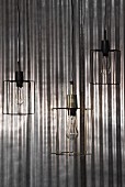 Three pendant lamps with minimalist wire lampshades in front of shiny corrugated metal background