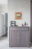 Decorative letters on top of rustic grey cabinet below sunburst mirror on stucco lustro wall