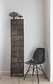 Dark grey classic shell chair next to tall, narrow, vintage metal cabinet in corner
