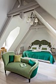 Antique recamier with green upholstery in front of double bed with curved headboard and deep-green blanket in attic room
