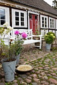 Zinc bucket of dahlias and bird bath on cobbles in front of white-painted garden bench and half-timbered house