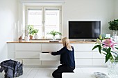 Woman in front of white fitted sideboard with drawers and flatscreen TV