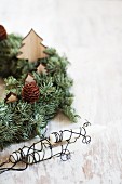 Wreath decorated with wooden Christmas trees next to candles wrapped in wire