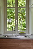 Water running from tap into sink below lattice window with view into garden
