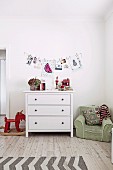 Children's room with white chest of drawers, rocking animal and green children's armchair, wall decoration with drawings and photos on a clothesline