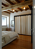 Double bed and walk-in wardrobe with a curtain door in bedroom with rustic wood-beamed ceiling
