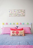Girl's room with pink pillowcases, pastel colored fairy lights on white headboard and bird motif on wall