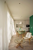 Wegner Shell Chair and glass table in lounge area with view of mint-green classic chairs in dining area and white, fitted designer kitchen