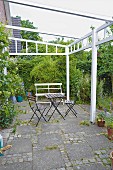 Gartenstühle und Tisch auf Terrasse mit weiss lackiertem Pergolagestell und Betonplatten