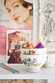 Sewing utensils in bowls with floral motifs in front of old fashion photographs