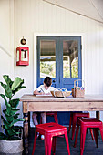Junge an rustikalem Holztisch mit roten Klassiker Hockern und Grünpflanze