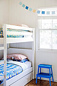 White bunk bed with colorful bed linen and blue step stool in front of window