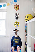 Boy with animal mask sitting on chair in white wood-clad children's room