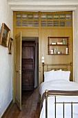 Antique brass bed against wooden wall with interior transom window and view of wooden cupboard in hallway