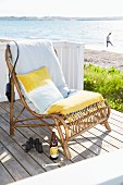 Yellow and white cushions on rattan easy chair on deck next to beach