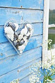 Love heart made from wire mesh and wire coathanger filled with shells and hung on board wall