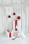 Gifts wrapped in red and white, red baubles and white X ornament in front of board wall