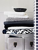 Stacked, monochrome towels on top of silver Oriental cabinet