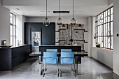 Dining table and blue chairs in open-plan kitchen of industrial loft apartment in shades of grey