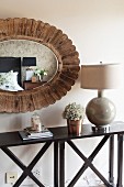 Oval mirror with wooden frame above console table with cross-braced frame