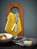 Yellow napkin and cutlery hanging from wooden board with hole