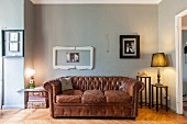Vintage leather sofa below picture frames on grey-painted wall and table lamps on small side tables