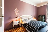 Schlafzimmer mit antikem Bett und schwarz-weiss gestreifter Bettwäsche, Fotodekoration an mauvefarbener Wand