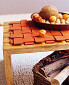 Autumnal arrangement on woven, orange felt mat on wooden table above basket of firewood