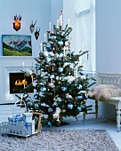 Christmas tree elegantly decorated with blue and white baubles in front of fireplace