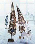 Lit pillar candles on white, stag-shaped candle holder in front of two small, wicker, Christmas tree ornaments