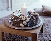 Rustikaler Adventskranz mit Naturmaterialen und weißer brennender Kerze auf Edelholztisch