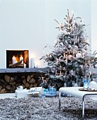 Weiß besprühter Christbaum mit weissen Kerzen und Glasschmuck dekoriert neben offenem Kamin