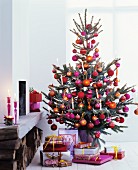 Presents below Christmas tree lavishly decorated with pink, red and orange baubles
