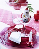 Festive place setting with red glass dishes embellished with Christmas tree decorations