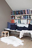 Scatter cushions on camp bed below bookcase under sloping ceiling
