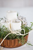 Pillar candles and evergreen twigs in copper cake tin